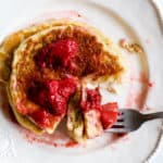 Stack of whole wheat protein pancakes on white plate with fork and bite taken out