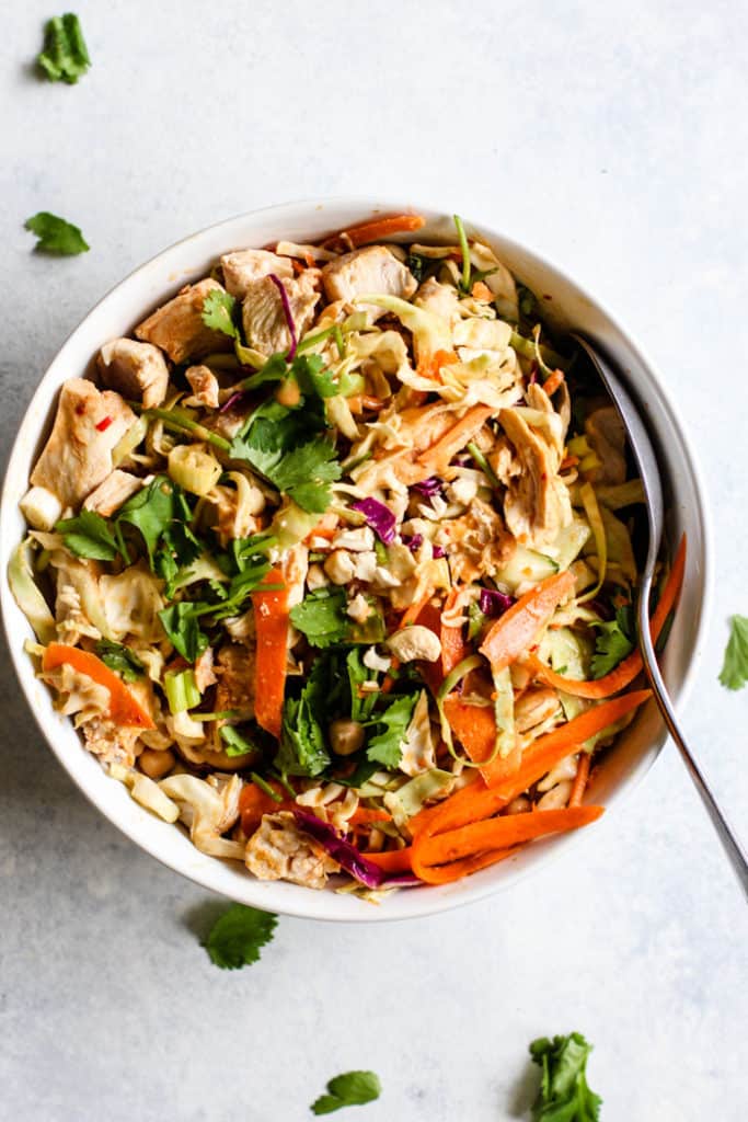 Thai peanut chicken salad with spicy peanut dressing in white bowl with spoon