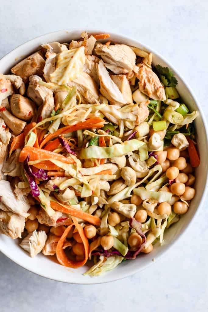 Thai peanut chicken salad ingredients in white bowl before tossing