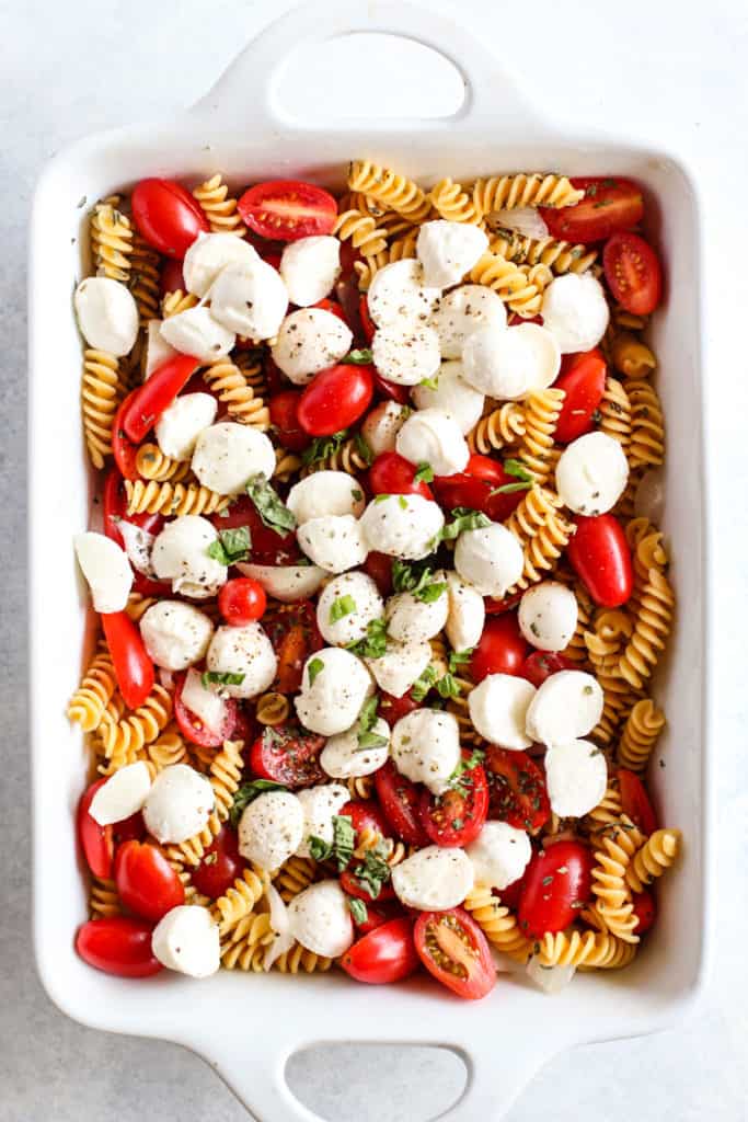 Simple caprese pasta bake ingredients in white ceramic dish prior to baking