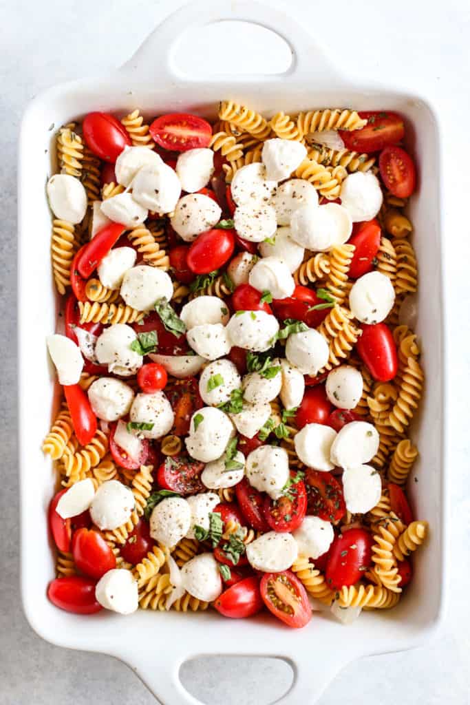 Simple caprese pasta bake ingredients in white ceramic dish prior to baking.