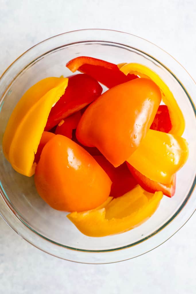 How to roast bell peppers prep: peppers in glass bowl tossed in olive oil and salt