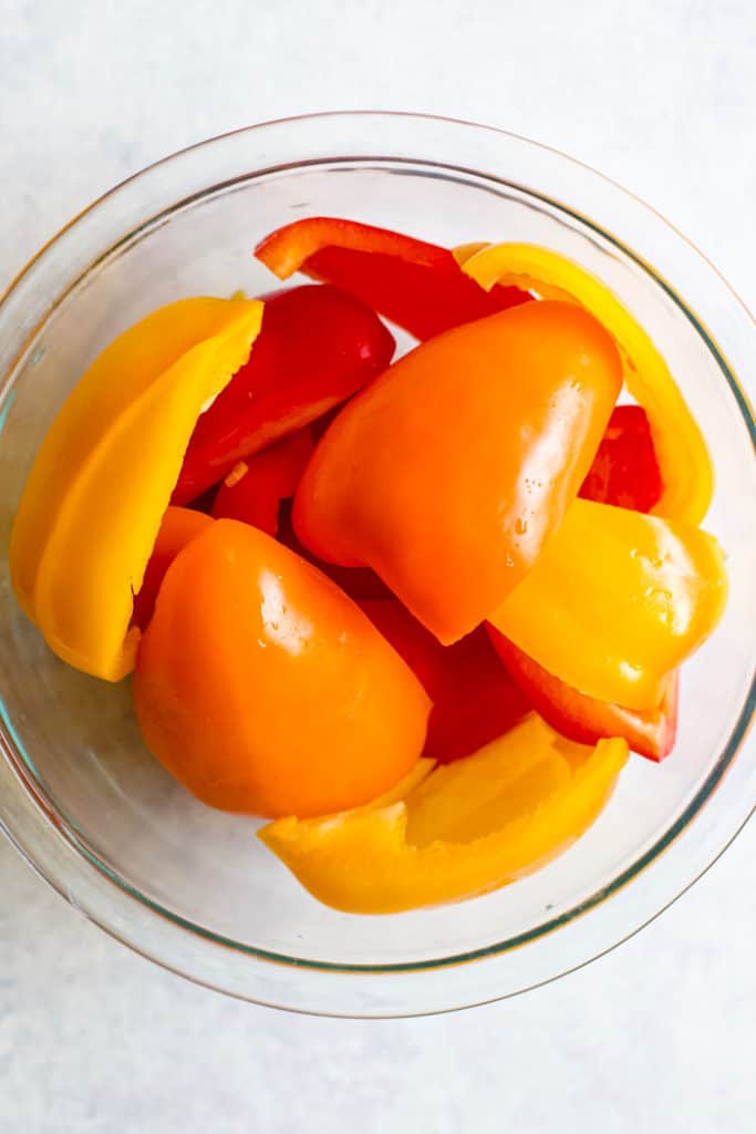 Red, orange, and yellow bell peppers in clear glass bowl.