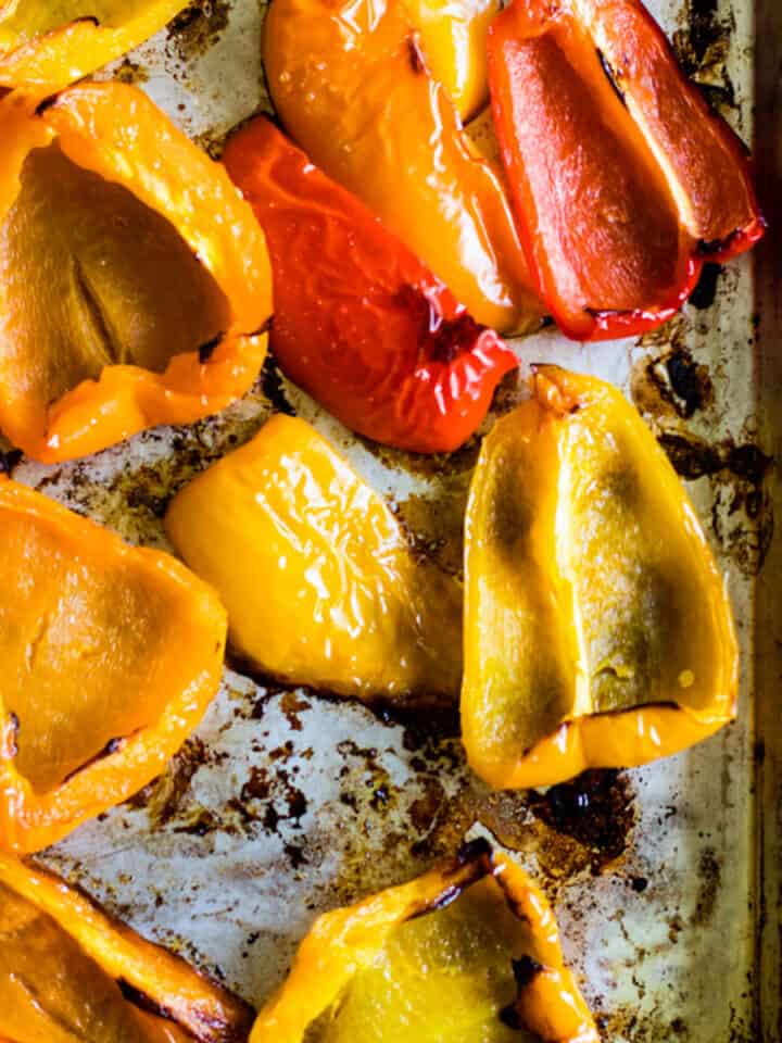 Roasted red, yellow, and orange bell pepper halves with nicely charred edges on sheet pan.