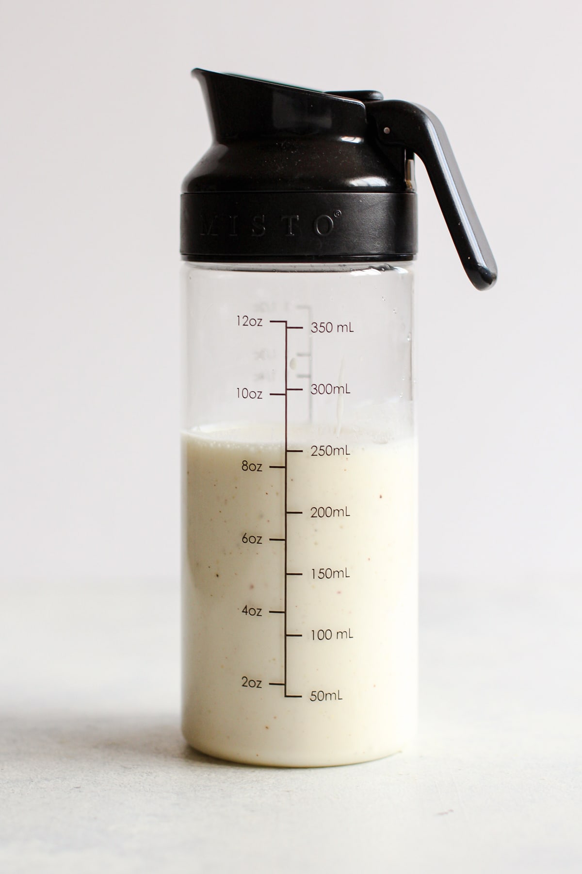 Creamy homemade Caesar dressing in measuring cup dressing container with black cover with handle and spout.