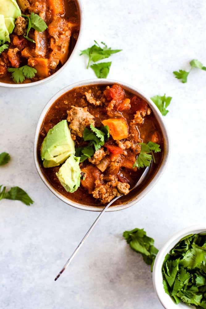 Sweet potato turkey chili in white bowl with cilantro and avocado topping