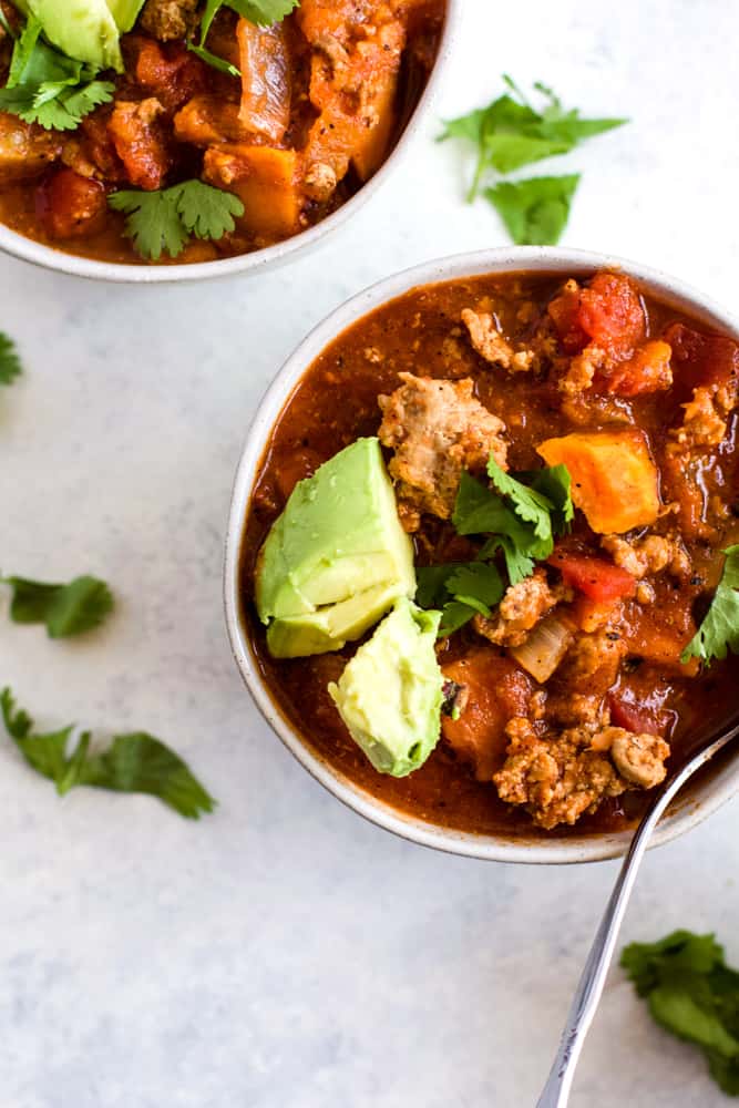 Sweet potato turkey chili in white bowl with cilantro and avocado topping