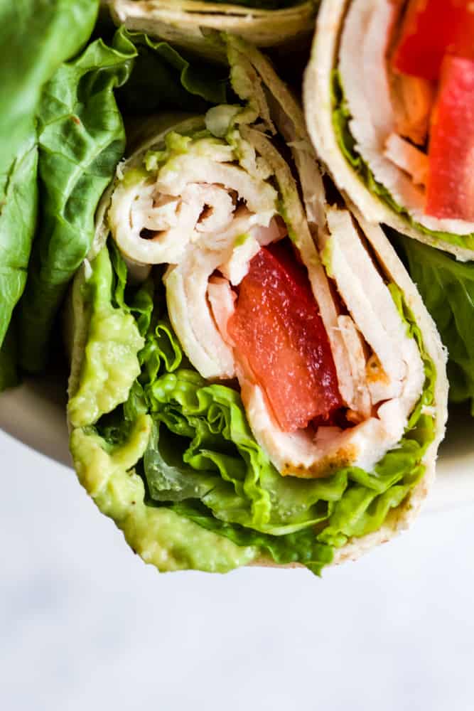 Whole wheat turkey wraps in white bowl with romaine lettuce leaves