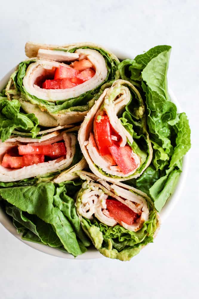 Whole wheat turkey wraps in white bowl with romaine lettuce leaves