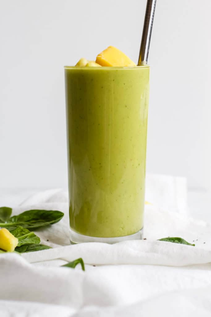 Pineapple mango avocado smoothie in tall glass with steel straw