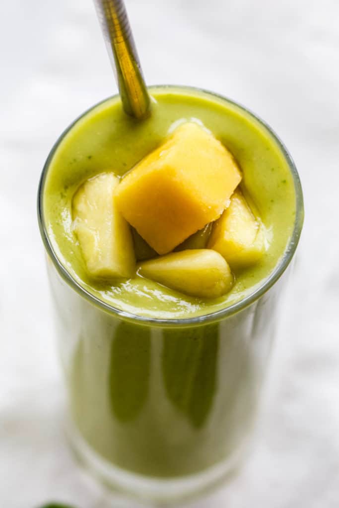 Pineapple mango avocado smoothie in tall glass with steel straw