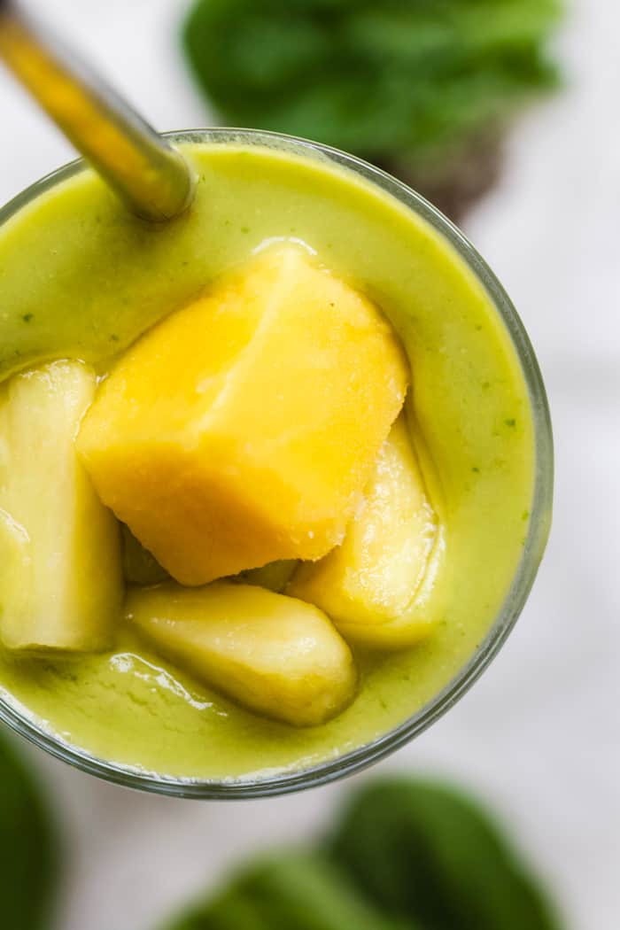 Pineapple mango avocado smoothie in tall glass with steel straw