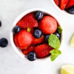 Honey lime mint watermelon berry salad in small white bowls on light surface with lime and blueberry