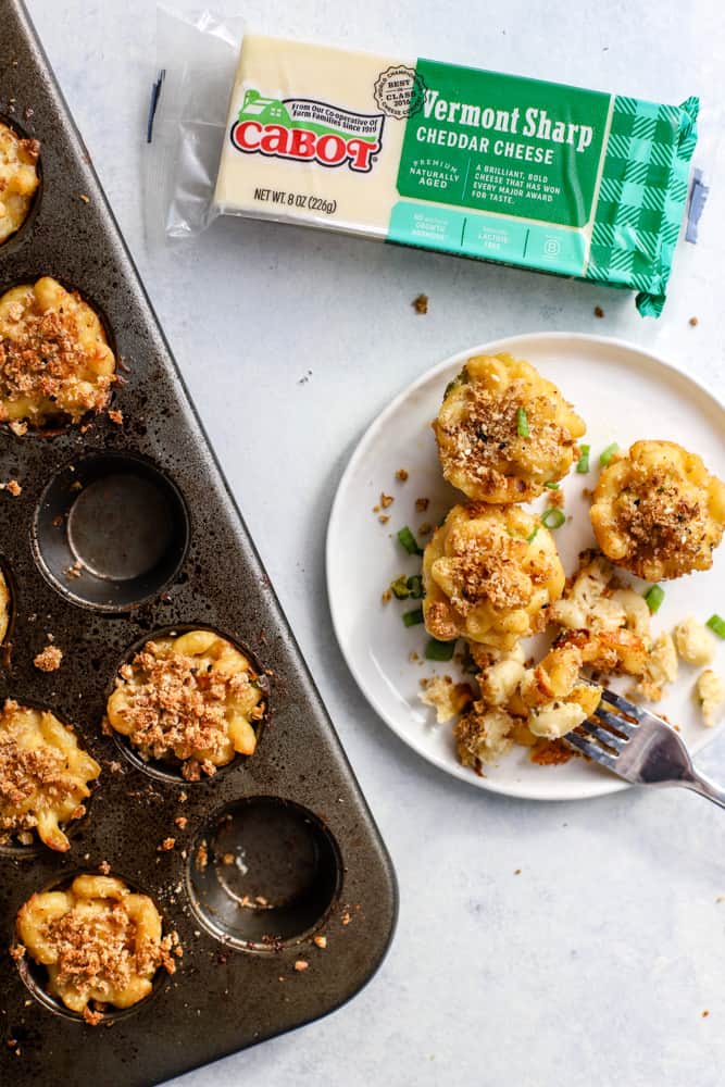 Healthy mac and cheese bites in mini muffin tin and on white plate, next to block of Cabot Cheese