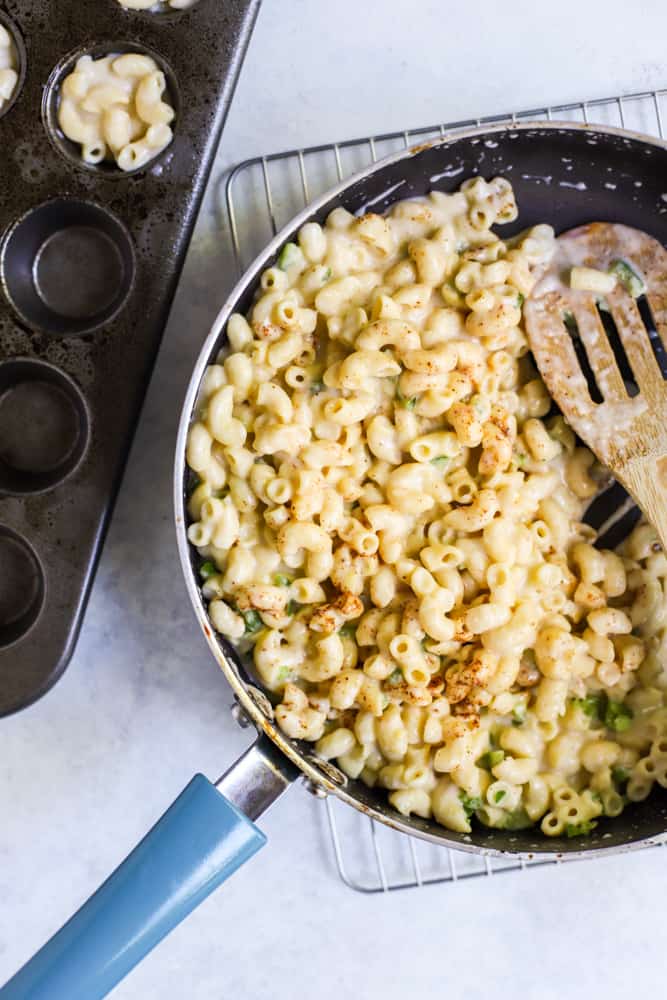 Mac and cheese with finely diced jalapeños and chipotle powder in sauté pan next to mini muffin tin
