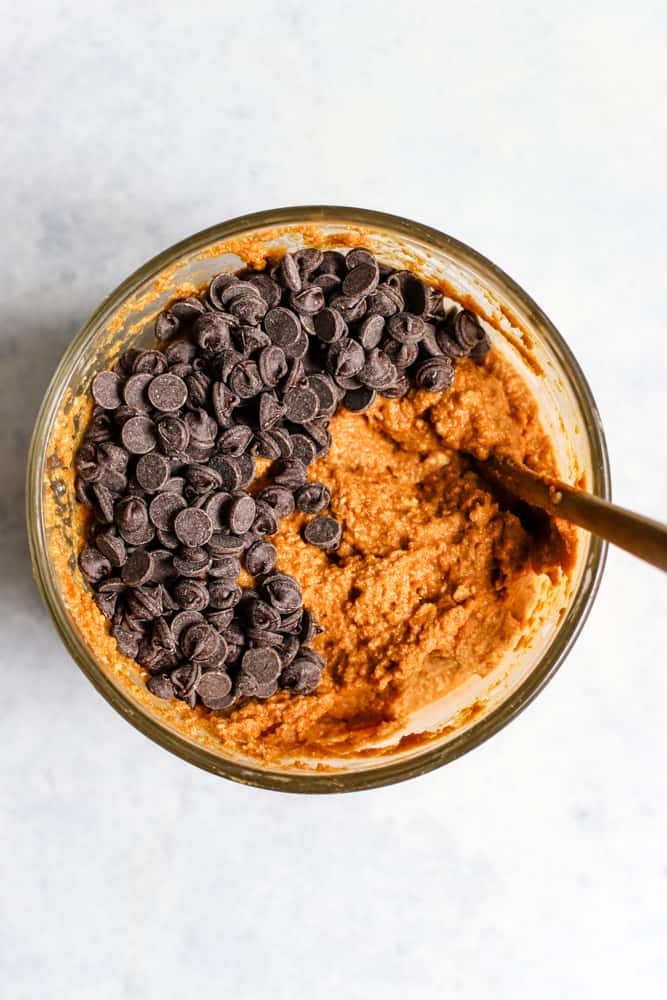 Pumpkin, egg, vanilla, butter, and maple syrup mixed together in clear mixing bowl with semi-sweet chocolate chips on top