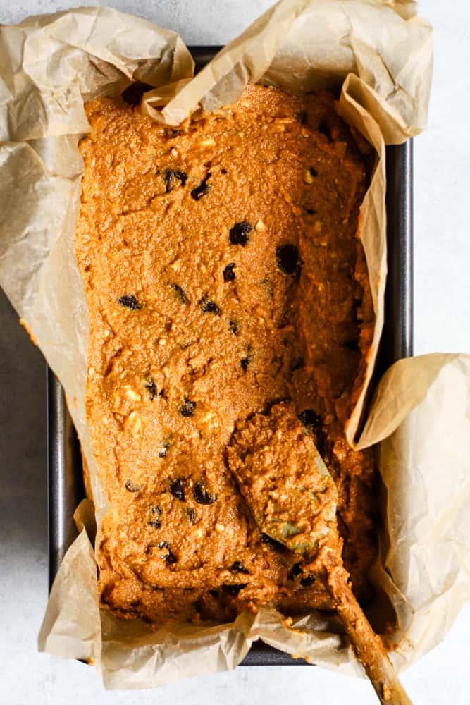 Pumpkin chocolate chip bread batter spread into loaf pan lined with parchment paper