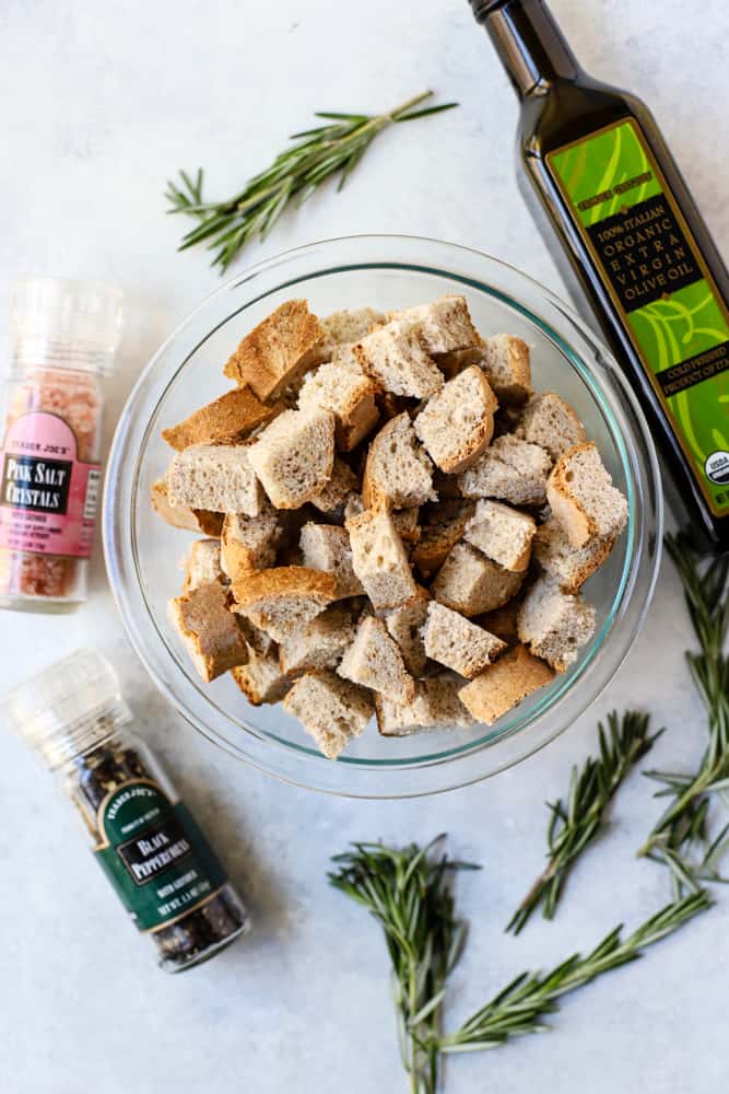 Bowl of bread cubes with bottle of olive oil, pink salt, pepper, and fresh rosemary sprigs