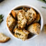 Baked croutons in small white bowl with rosemary sprigs in background