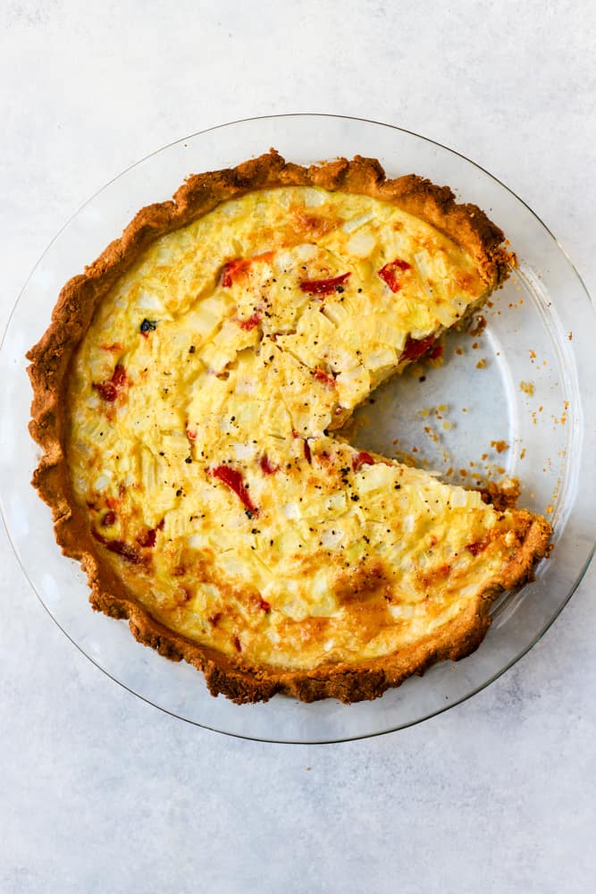 Simple quiche with chickpea flour baked in clear glass pie dish with slice taken out