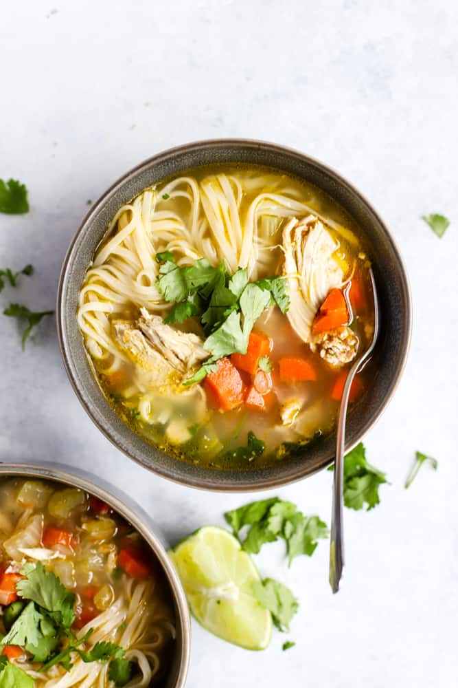 Ginger lime chickek noodle soup in dark gray bowl garnished with cilantro, on light blue surface