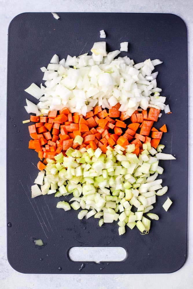 Chopped onion, carrots, and celery on black cutting board