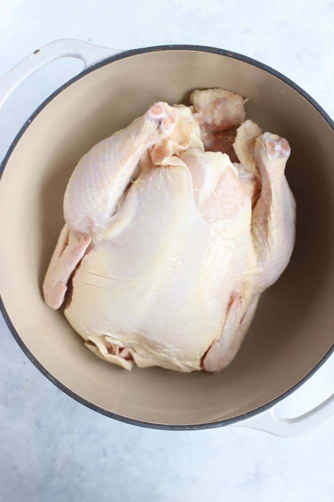 Whole uncooked chicken in white dutch oven