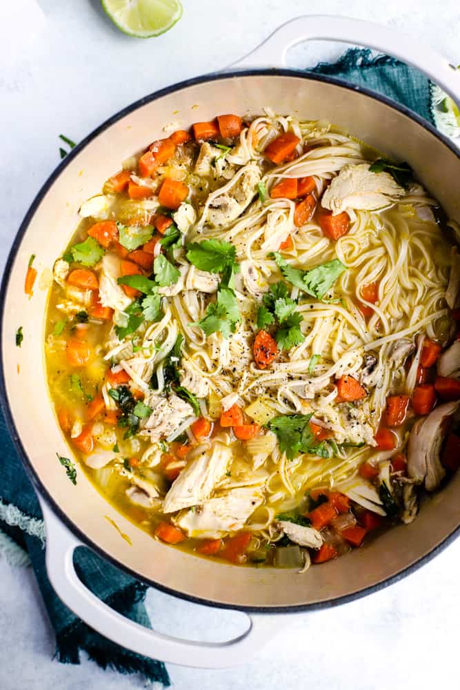 Ginger lime chicken noodle soup with cilantro sprinkled on top in large white dutch oven