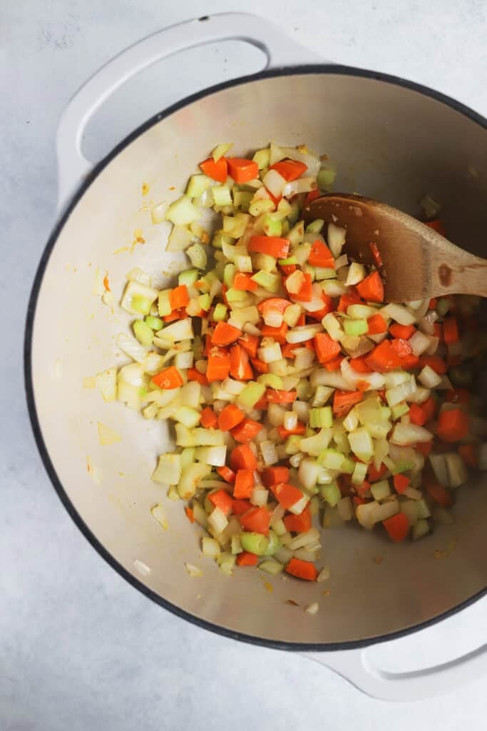 Sautéing carrots, celery, onions, garlic, and ginger in a dutch oven.