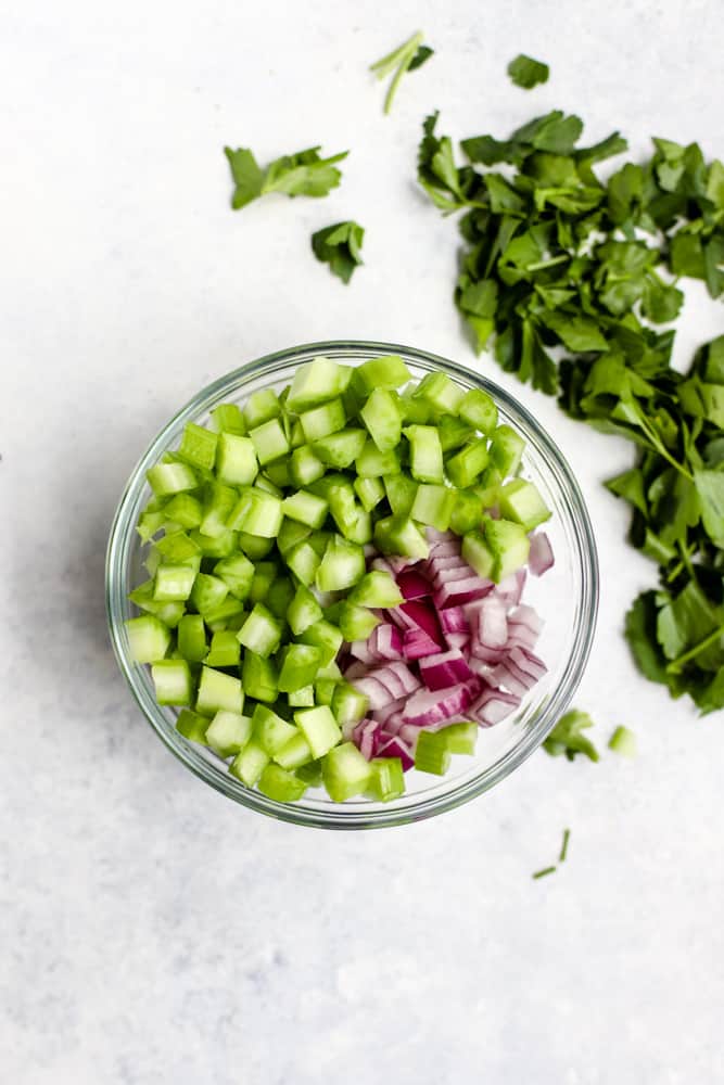 Small diced celery and red onion in a small clear glass bowl with some chopped parsley on the side