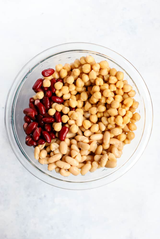 Kidney beans, cannellini beans, and chickpeas, drained and rinsed, in a clear glass bowl