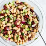 Modern three bean salad ingredients all in a clear glass bowl, tossed in creamy apple cider vinaigrette and topped with freshly cracked black pepper