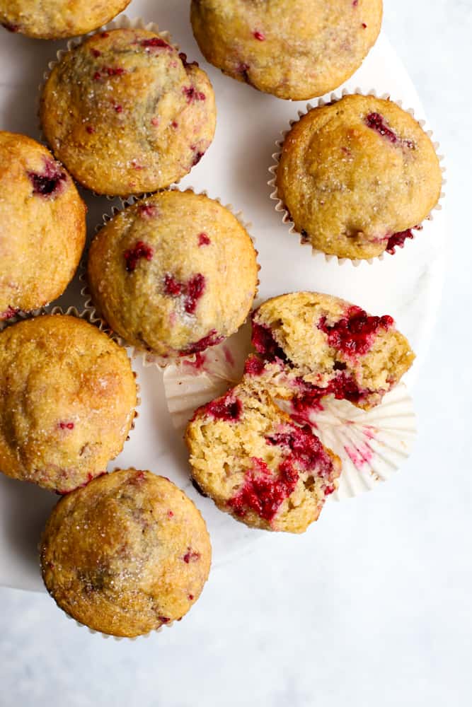 Wholesome raspberry lemon muffins in white marble cake stand with one muffin cut in half, lying open, and tender insides showing