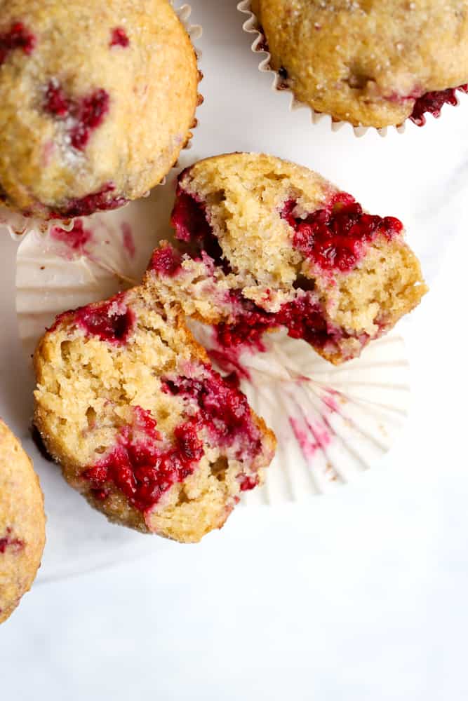 One wholesome raspberry lemon muffin cut open on white marble cake stand, with tender inner crumb and juicy raspberries showing