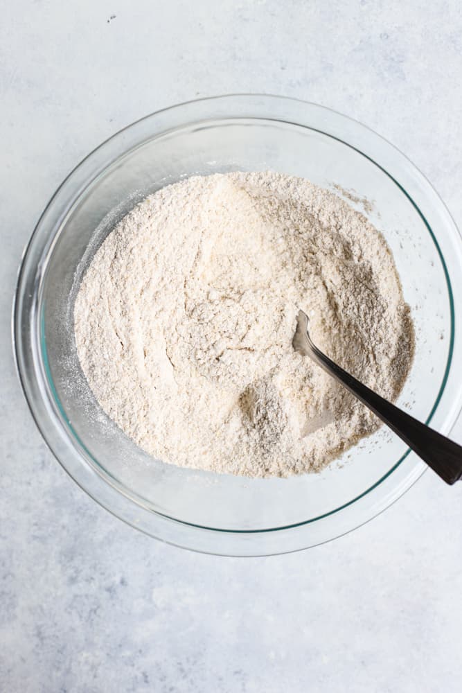 Flour, baking soda, baking powder, and salt whisked together in a clear bowl with a fork