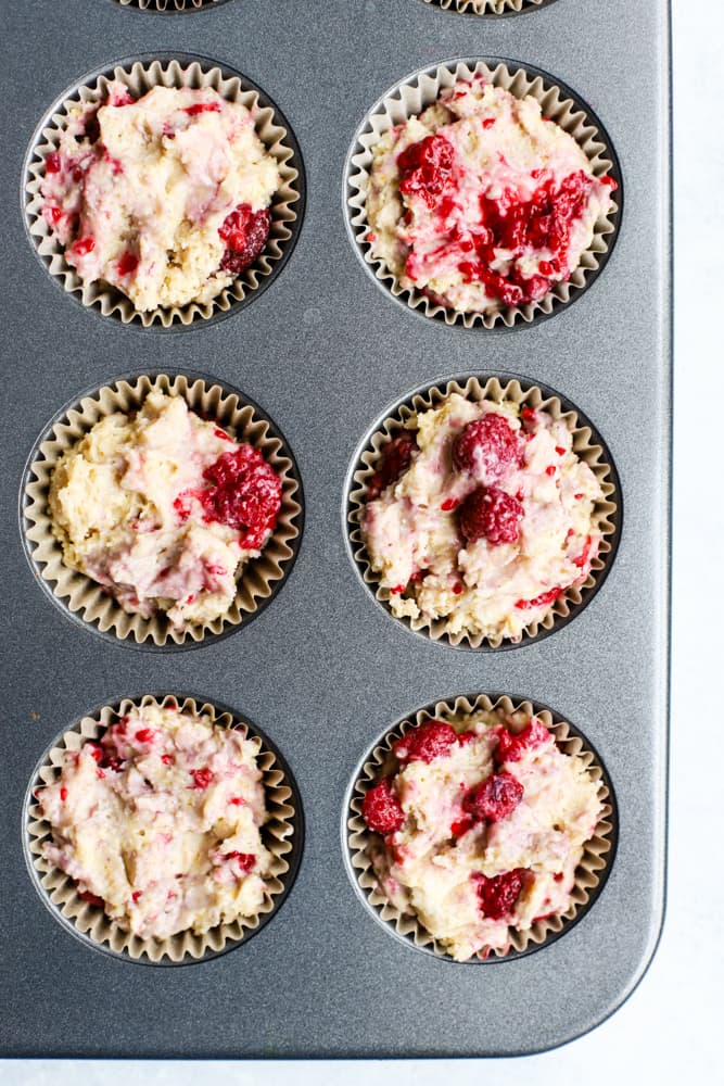 Raspberry lemon muffin batter evenly distributed into parchment paper muffin cups in muffin tin
