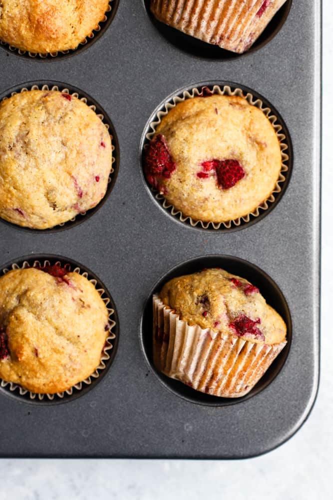 Baked wholesome raspberry lemon muffins in muffin tin with some muffins tilted to side