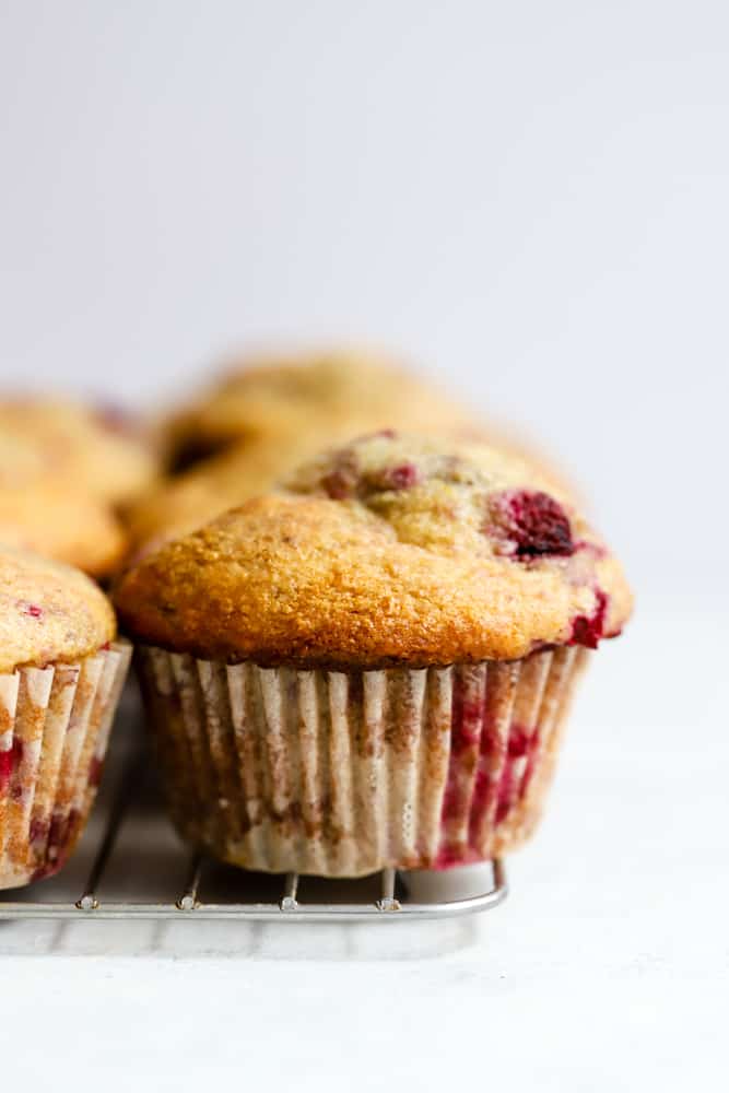 Baked wholesome raspberry lemon muffins on cooling rack on white and light blue surface