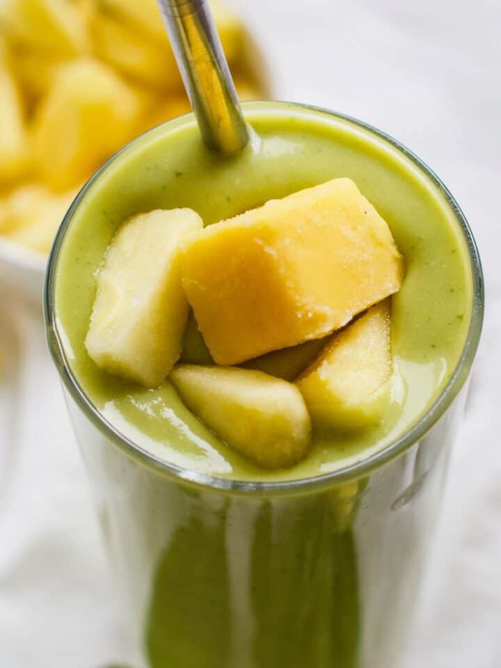 Mango pineapple avocado protein smoothie in tall glass with straw.