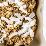 Simple coconut chia granola on parchment paper lined sheet pan with coconut just added before putting back in oven to toast