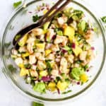 Shrimp mango and avocado salad in clear bowl with copper serving spoon set on light blue and white background