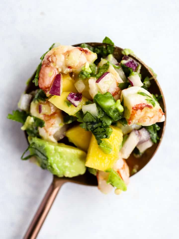 Shrimp mango and avocado salad in copper serving spoon on white and light blue background