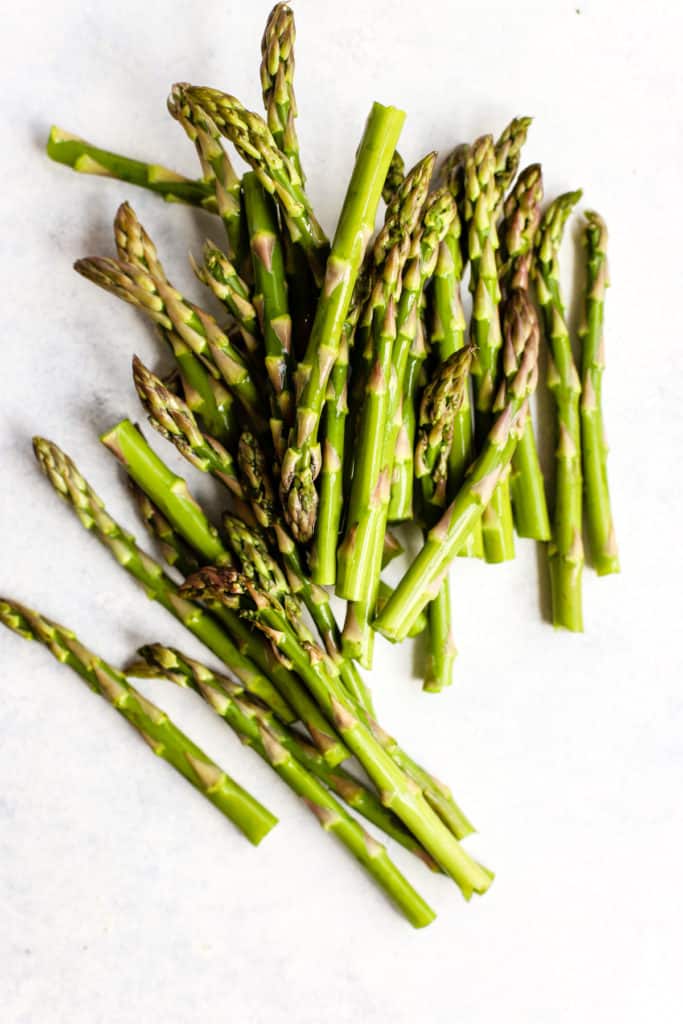 Fresh asparagus spears spread out on light blue and white surface.