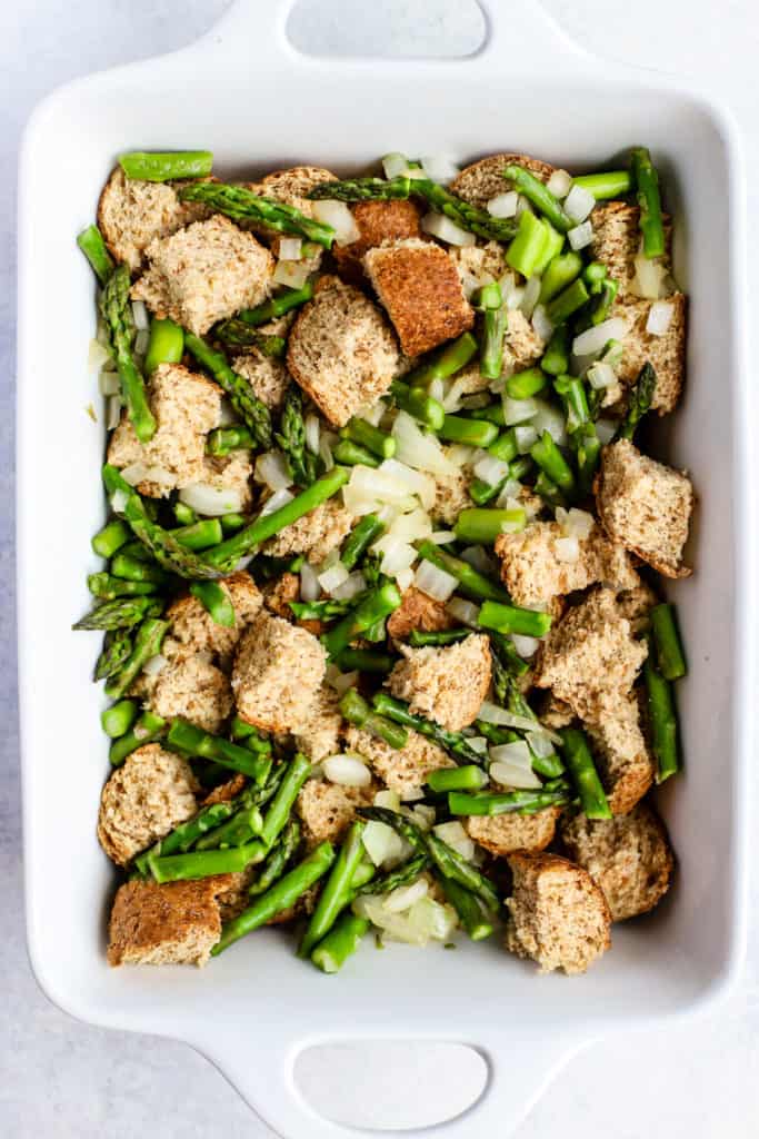 Bread cubes, asparagus, and onion in white ceramic baking dish.