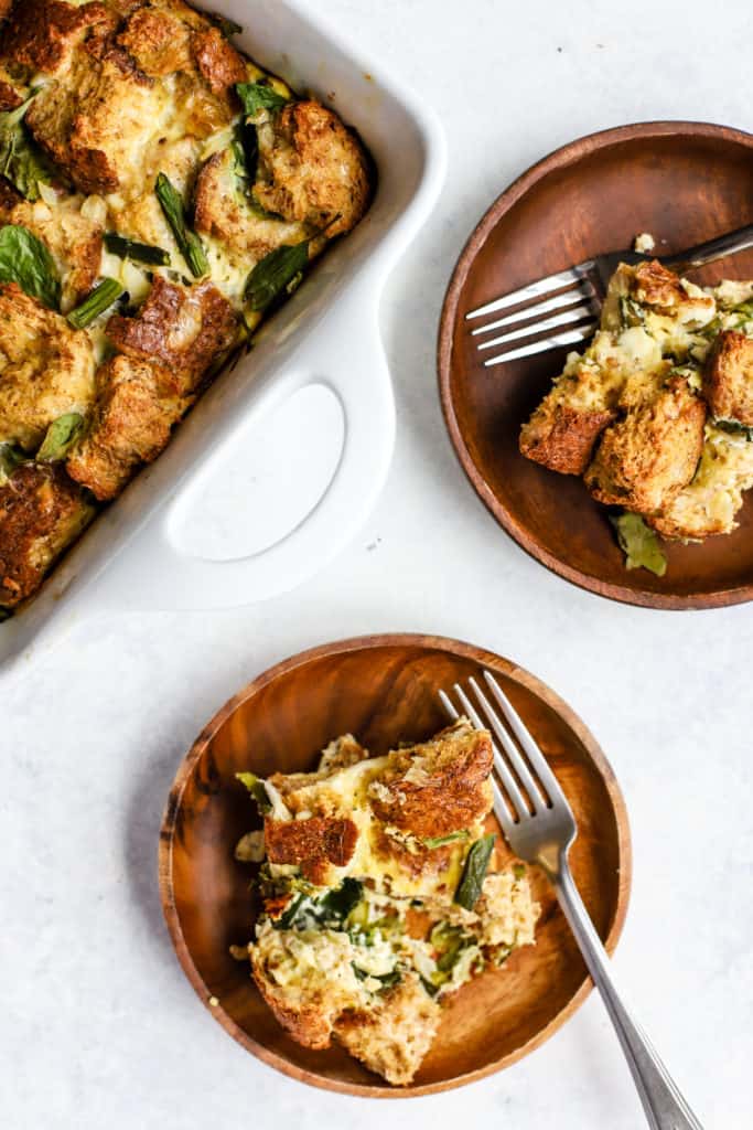 Healthy spring veggie breakfast strata squares on two wooden plates with forks.