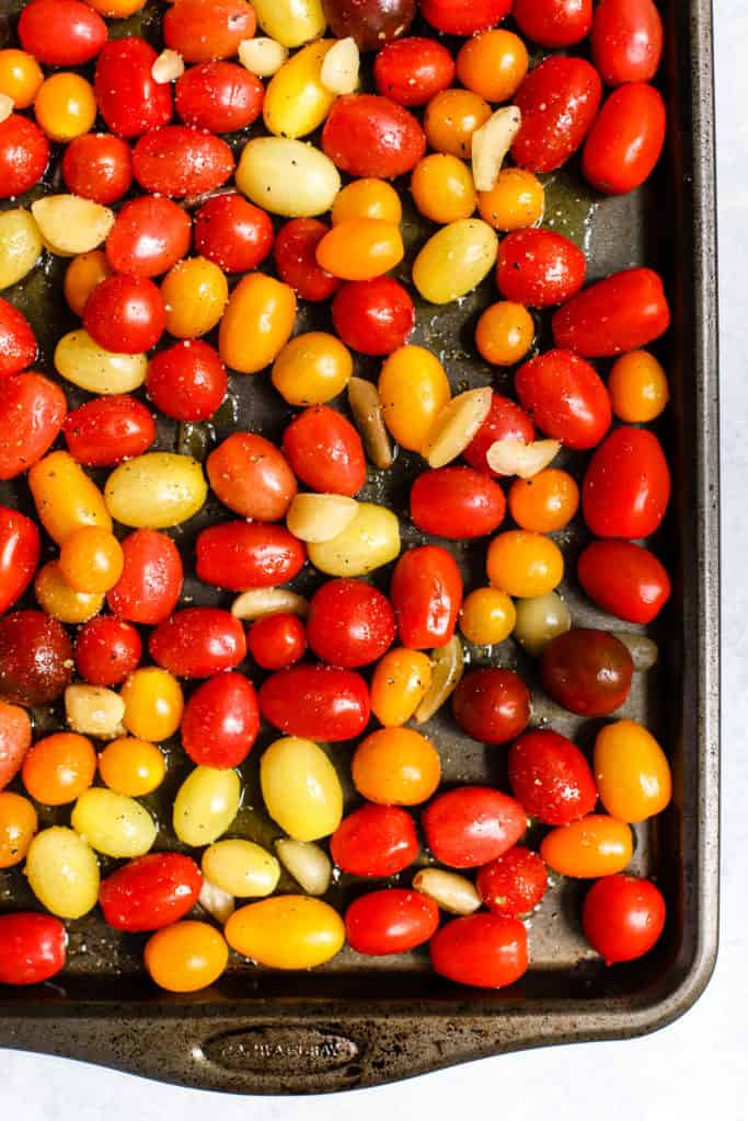 Cherry and grape tomatoes and garlic cloves with olive oil, salt, and pepper on sheet pan