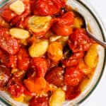 Garlic roasted tomatoes in clear glass container with spoon