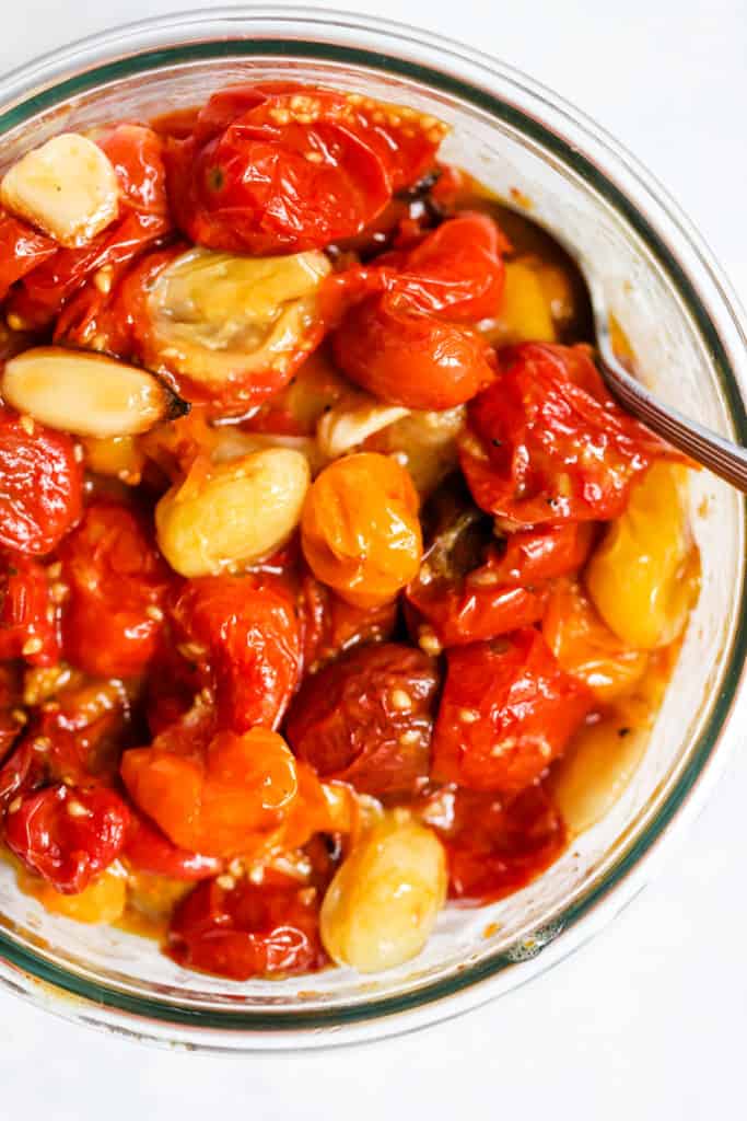 Garlic roasted tomatoes in clear glass container with spoon