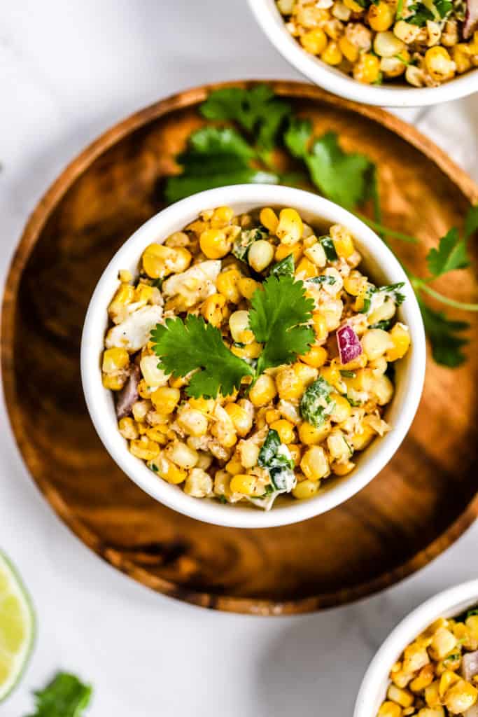 Healthy Mexican street corn salad in white bowl on wooden plate with fresh cilantro garnish