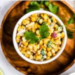 Healthy Mexican street corn salad in white bowl on wooden plate with fresh cilantro garnish